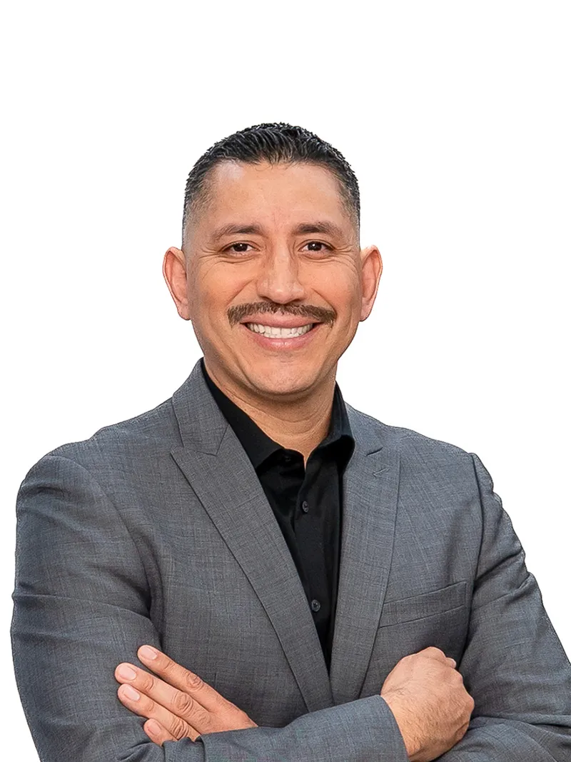 Corporate headshot of a man in a gray suit with arms crossed against a white studio backdrop