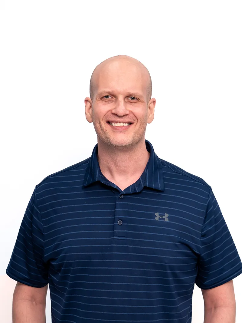 Corporate headshot of a man in a striped polo shirt against a white studio backdrop