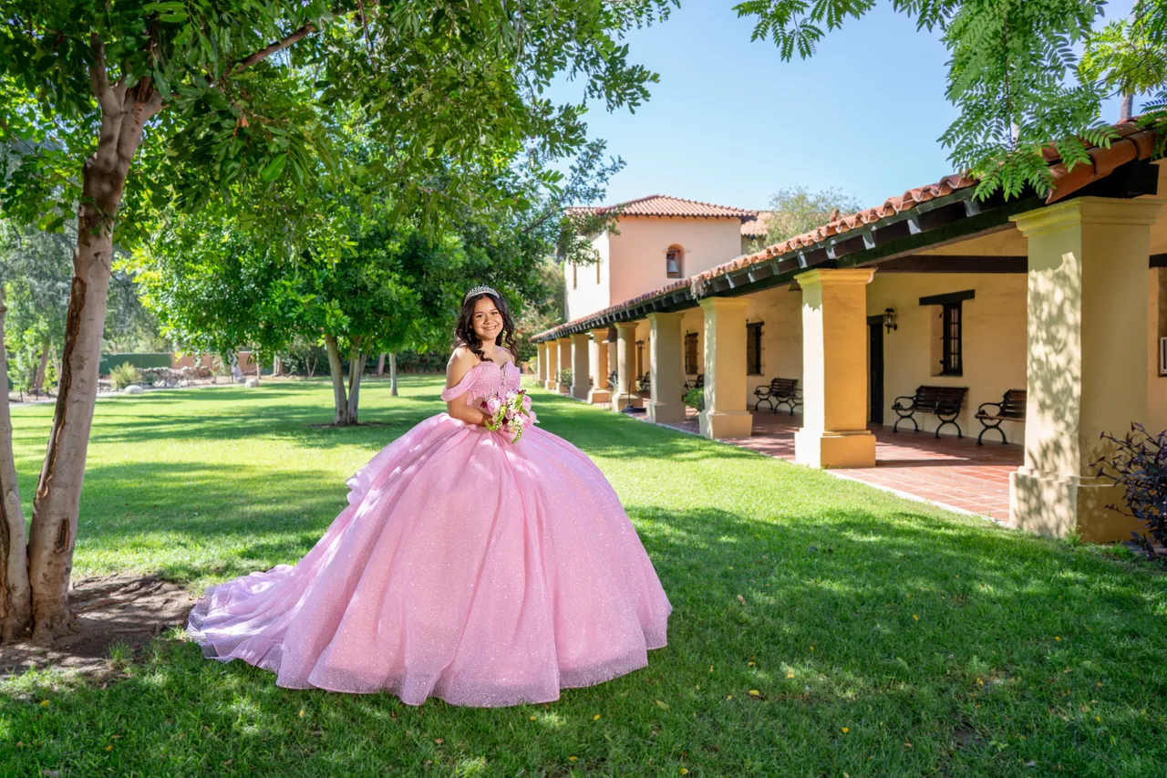 Quinceañera in a pink ballgown outside a mission-style building