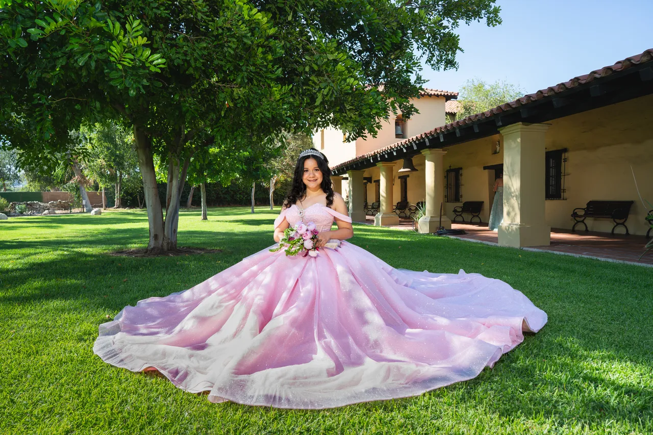Quinceañera in a pink ballgown posing in a garden setting