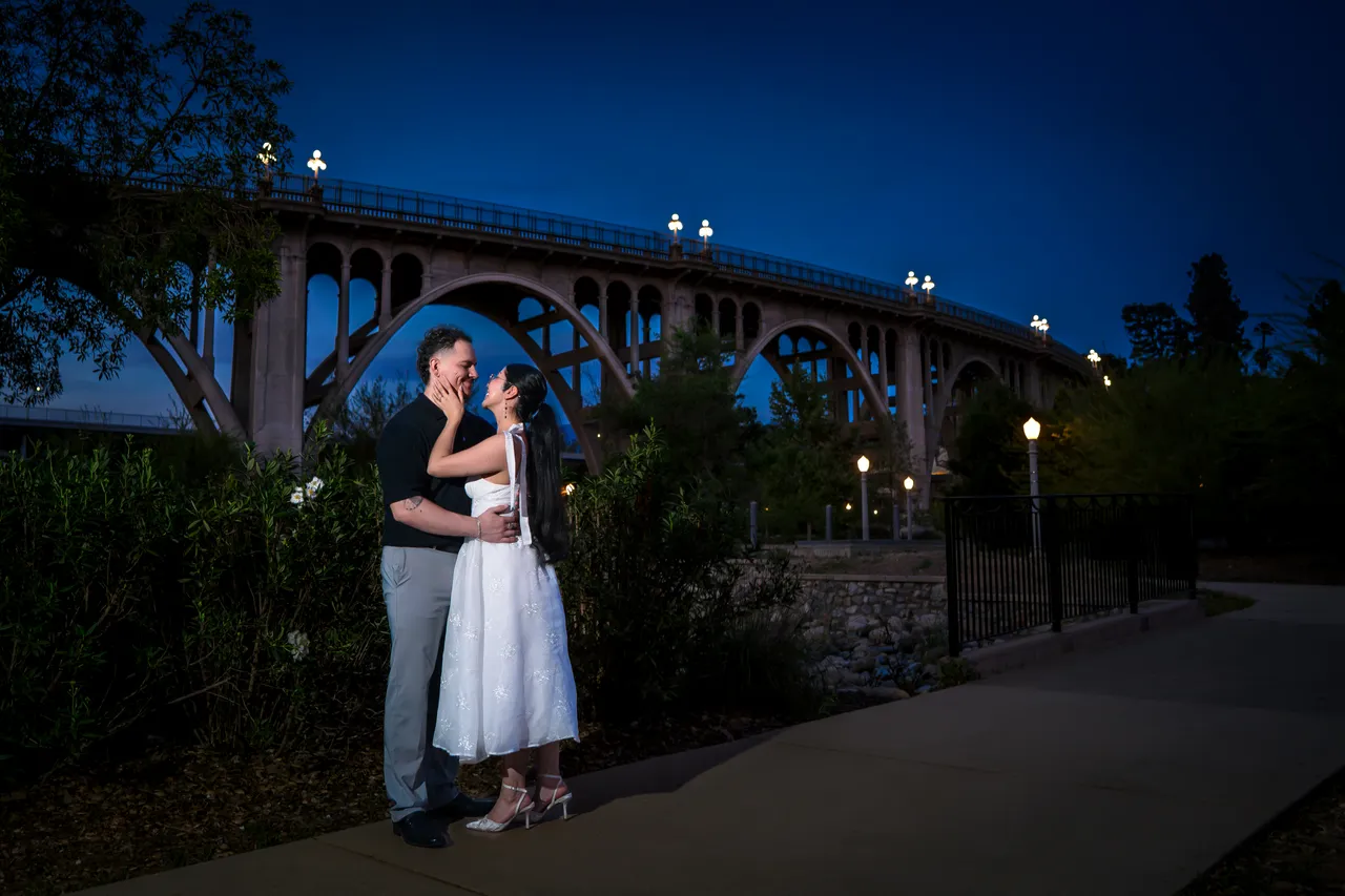 Couple embracing under a tall arched stone bridge at dusk, Colorado Street Bridge, Pasadena